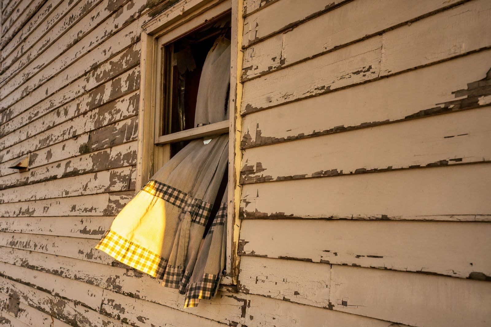 Weathered wooden siding beside an open window with a curtain