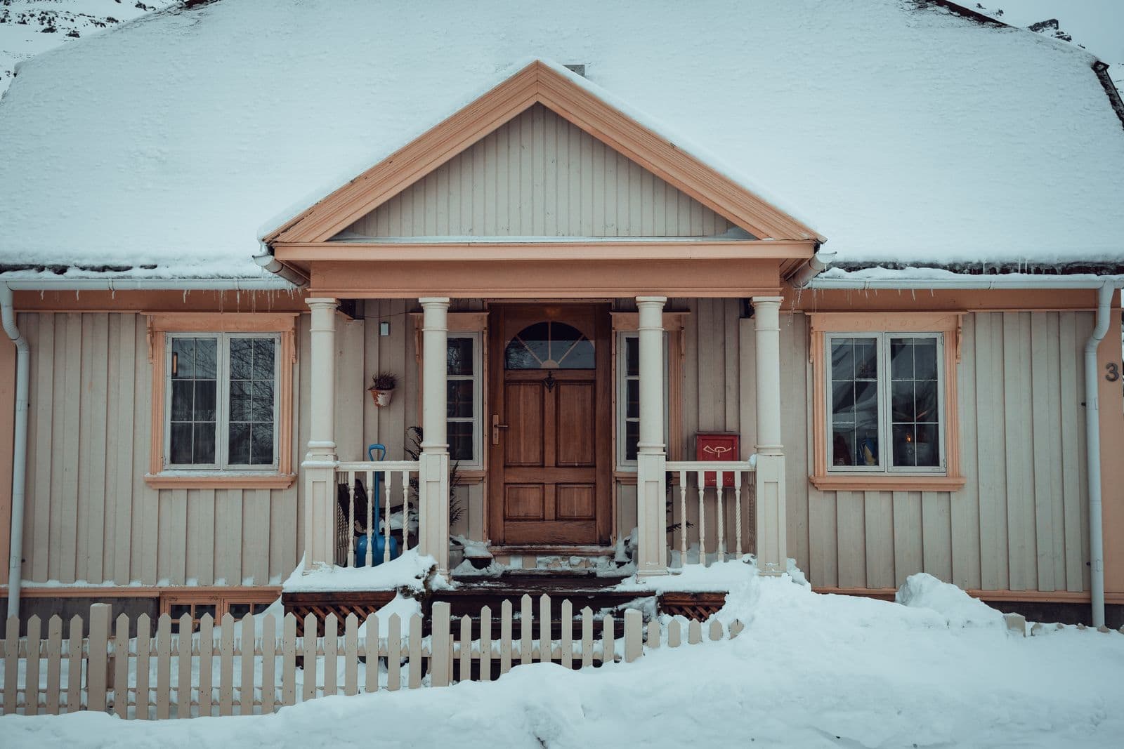 Cottage with lap siding and a front porch under a snowy roof